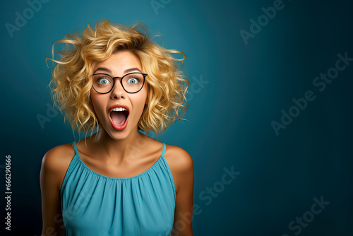 Studio portrait of a blonde girl with beautiful blue eyes in blue t-shirt and glasses opening her mouth in surprise
