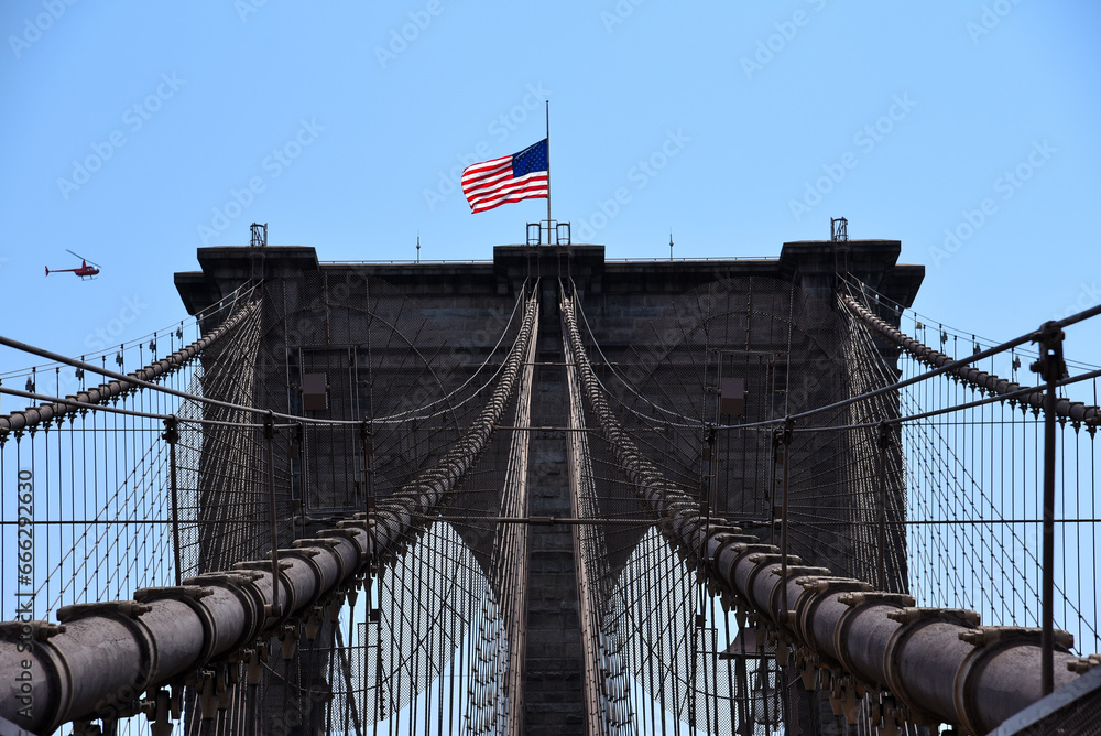 Fototapeta premium The American Flag by the Wind over Brooklyn Bridge - New York City, USA