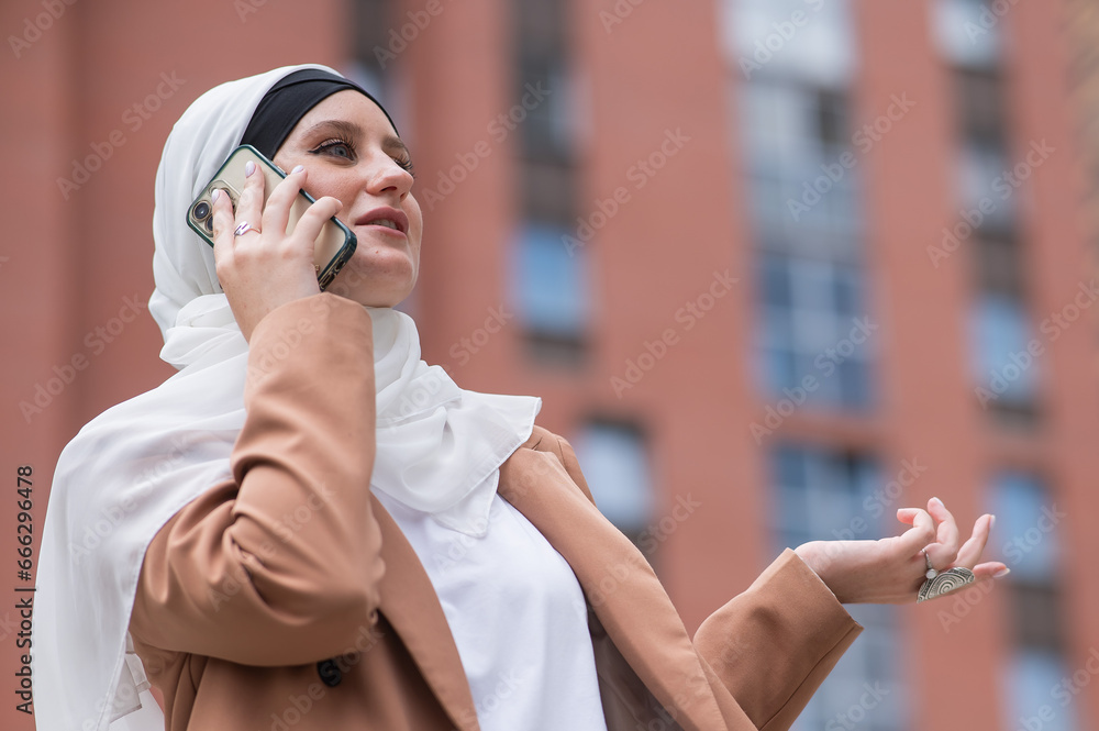 Young woman in hijab talking on smartphone outdoors. 