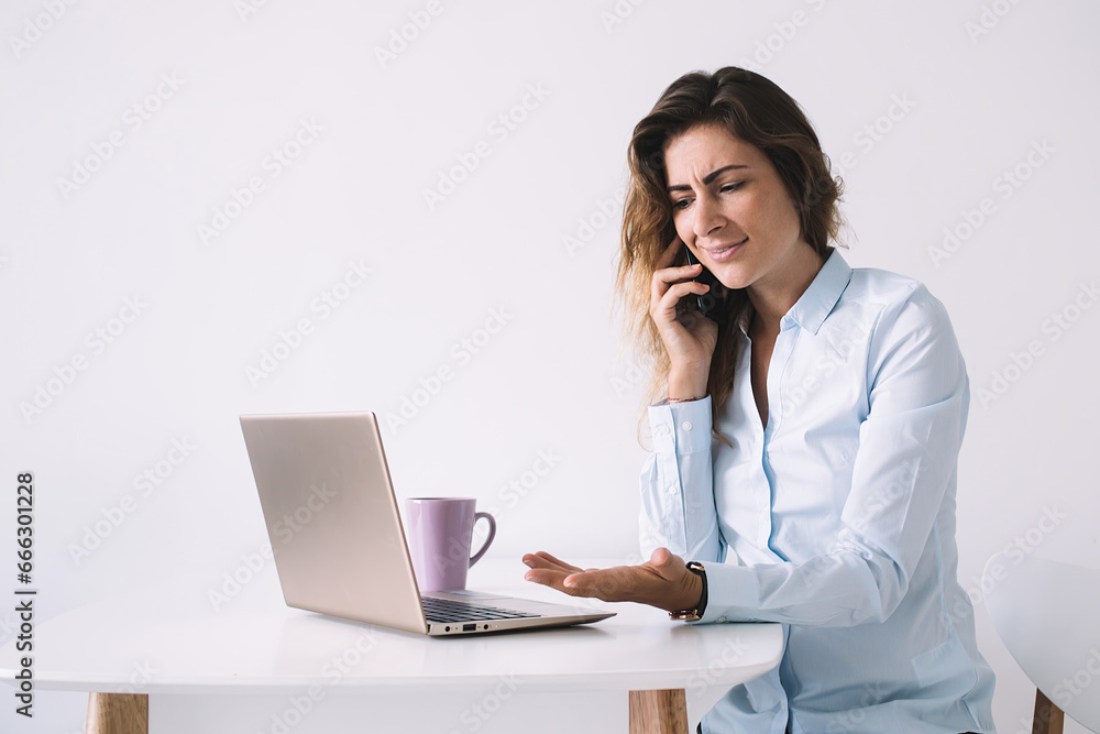 Confused woman talking on phone and watching laptop Confused woman talking on phone and watching laptop