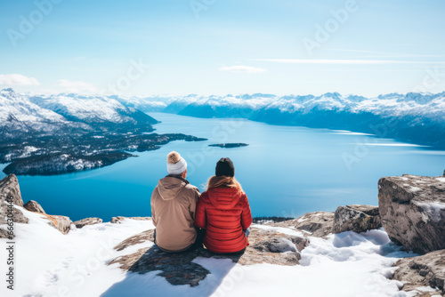 A couple sitting at the top of a snowy mountain, view from the behind. A winter hiking and wanderlust concept