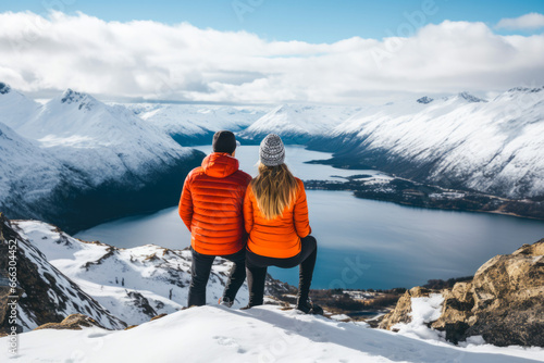 A couple sitting at the top of a snowy mountain, view from the behind. A winter hiking and wanderlust concept