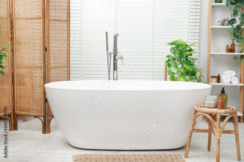 Spa day. Stylish bathroom interior with ceramic tub and green houseplants