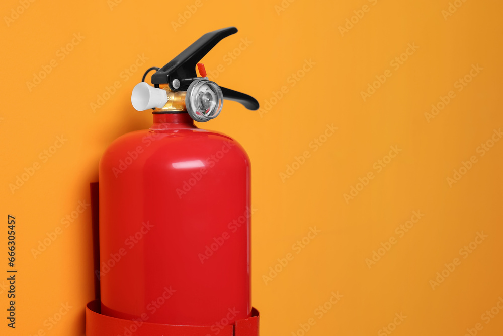 Red fire extinguisher on orange background. Space for text Red fire extinguisher on orange background. Space for text