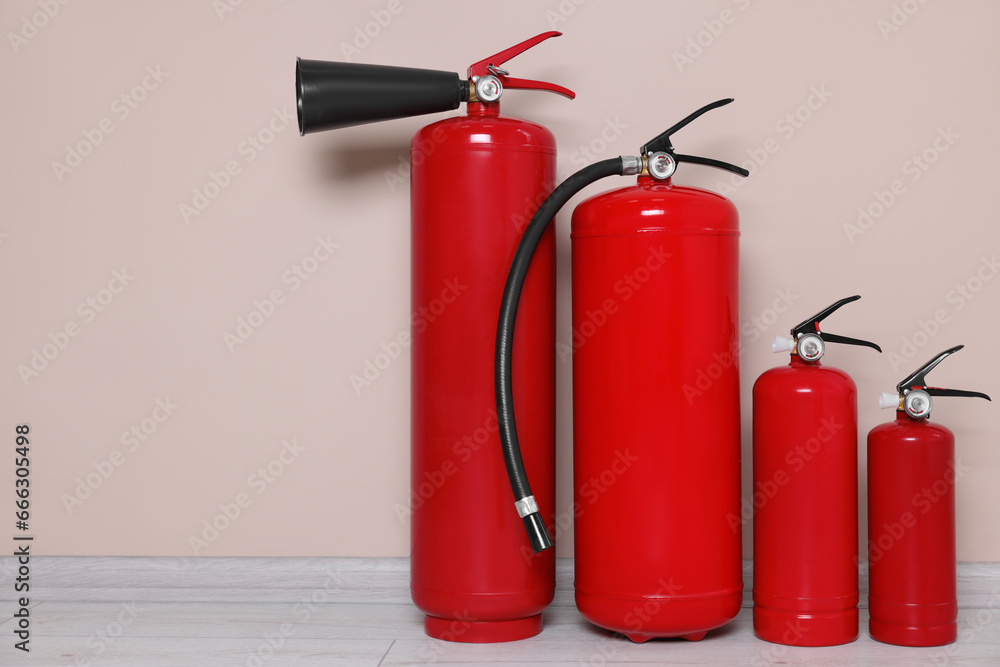 Set of fire extinguishers on floor near beige wall, space for text
