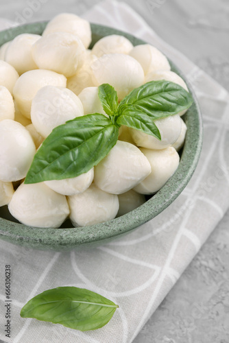 Tasty mozzarella balls and basil leaves in bowl on grey table