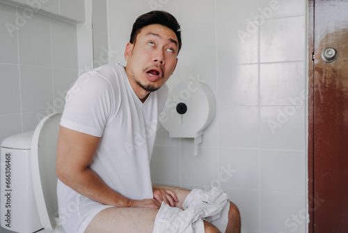 Funny face asian man pushing poop in the toilet as he has constipation. photo