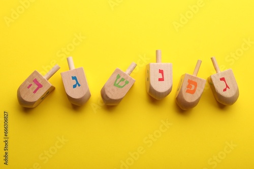 Wooden dreidels on yellow background, flat lay. Traditional Hanukkah game photo