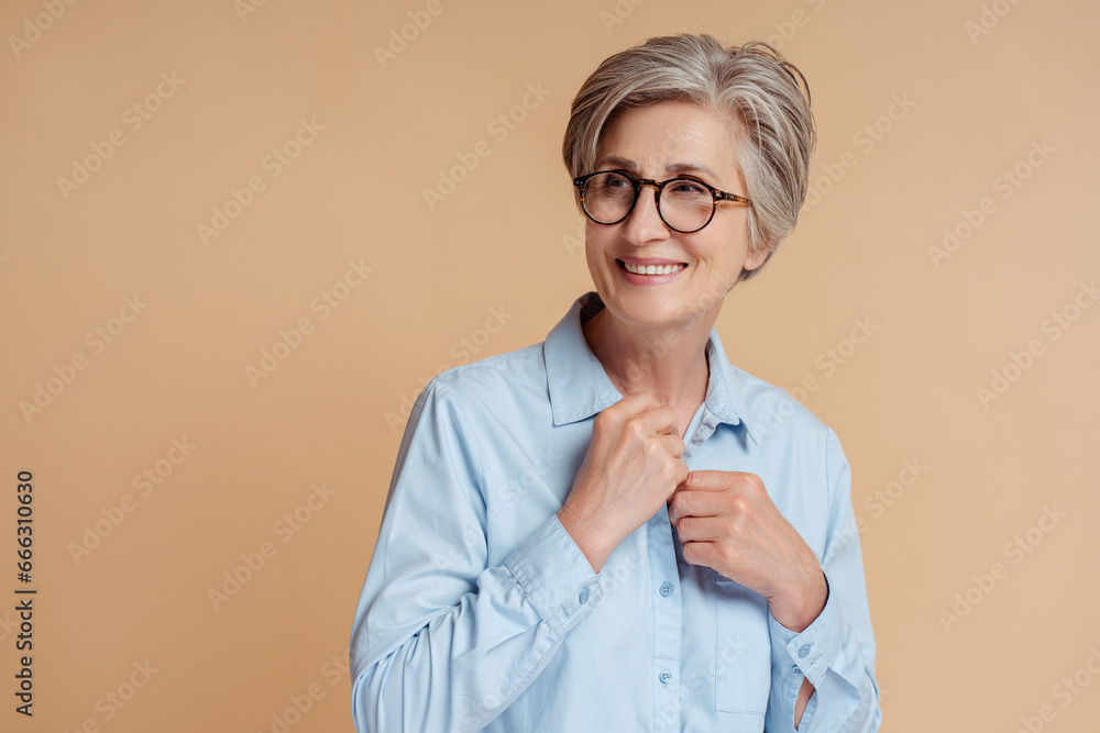 Portrait of beautiful senior woman wearing stylish glasses looking away isolated on beige background, copy space.  Vision concept