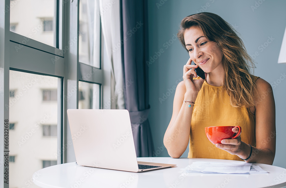 Glad female sitting at table with notebook and cup talking on mobile Glad female sitting at table with notebook and cup talking on mobile