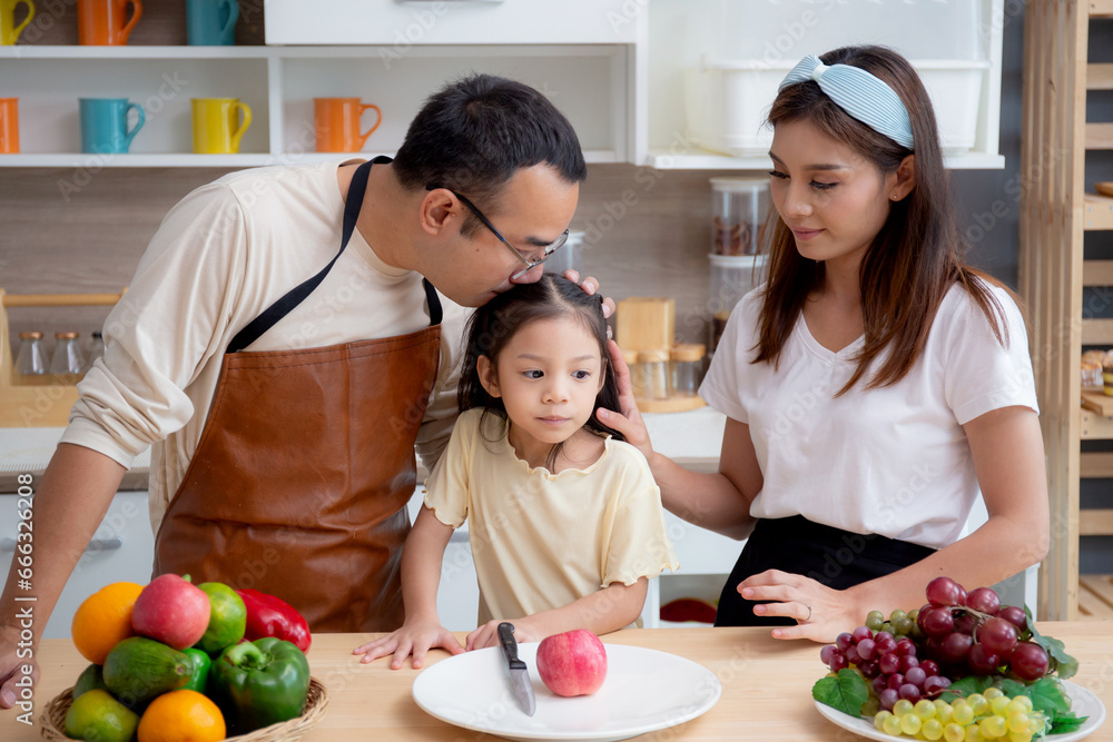 Happy family with father, mother and daughter in kitchen while mother chop apple fruit together at home, happiness mom, dad and child with bonding and relation, lifestyles and nutrition concept.