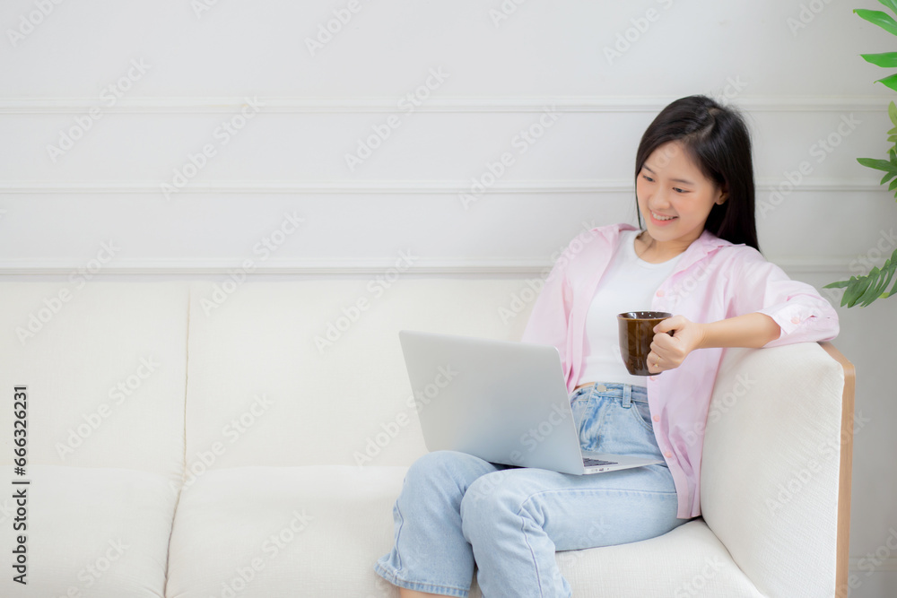 Young asian business woman work from home with laptop computer and drinking coffee on sofa in living room, freelance girl using notebook sitting on couch with comfort and relax, lifestyles concept.