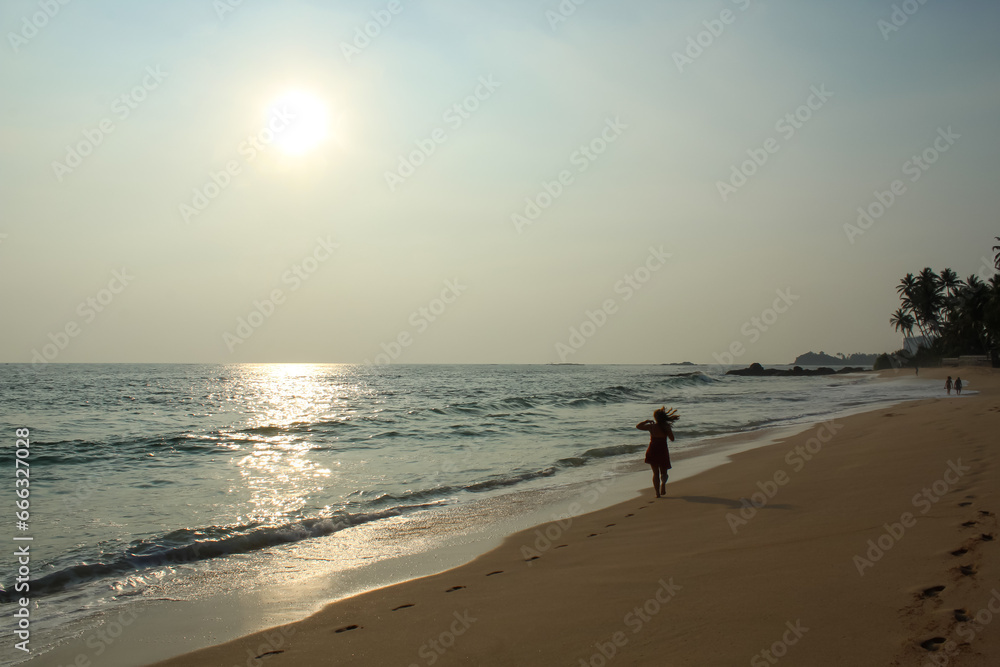 Wild raw empty beach in Sri Lanka with a girl wearing red dress