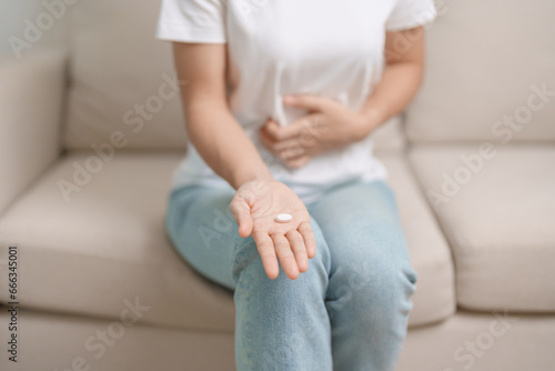 woman hand holding medicine painkiller pill and water glass on the sofa at home, taking for headaches,  stomach ache, Diarrhea Pain from food poisoning, Endometriosis, Hysterectomy and Menstrual