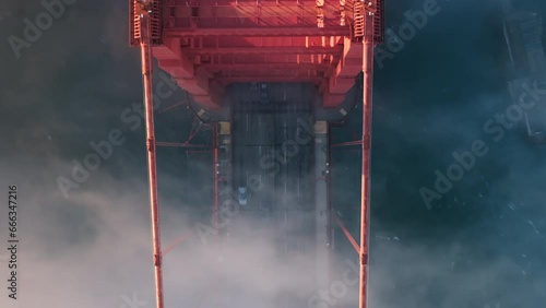 Vehicles driving by Golden Gate Bridge road at foggy sunset. Aerial top down view of misty golden cloud busy road above deep blue Pacific ocean. Famous tourist attraction of San Francisco, California