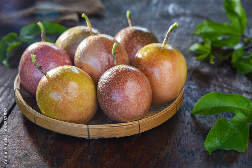 Passion fruit (Maracuya) in a bamboo tray with green leaves on a wooden table background.