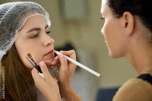 Master of permanent makeup draws a sketch of the work on the lips of a young model. The process of creating a sketch of lip tattooing with a special colored pencil before the procedure