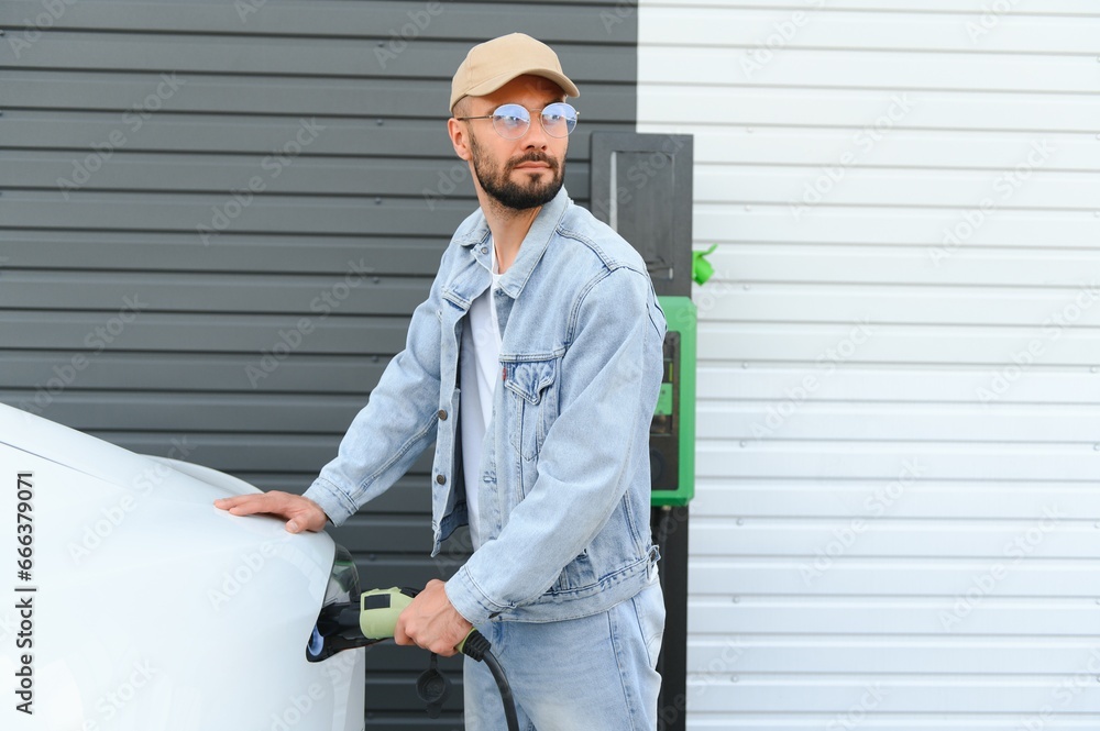 Stylish man inserts plug into the electric car charging socket Stylish man inserts plug into the electric car charging socket
