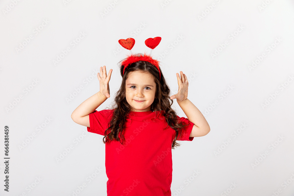 Smiling happy little girl in red t-shirt and headband with two red hearts celebrating Valentine's day on white. children's holiday card, gift for Mother's day, Father's day, hobby, crafts concept. Smiling happy little girl in red t-shirt and headband with two red hearts celebrating Valentine's day on white. children's holiday card, gift for Mother's day, Father's day, hobby, crafts concept.