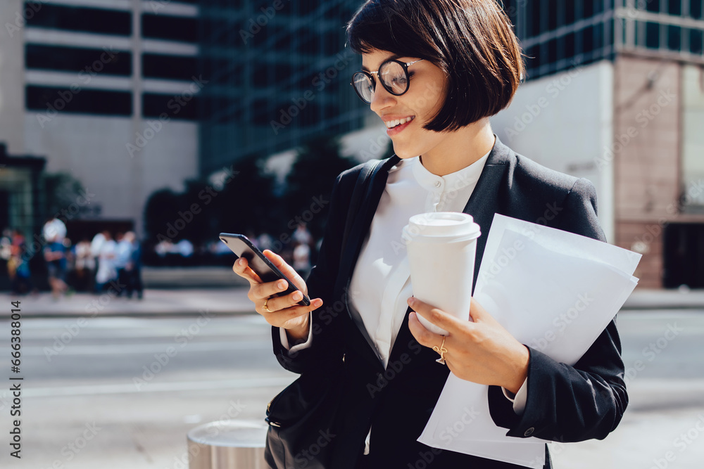Smiling female owner reading funny message via smartphone while standing on modern street Smiling female owner reading funny message via smartphone while standing on modern street