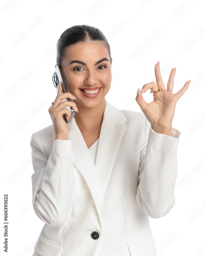 excited elegant girl in white suit talking on the phone and making ok gesture excited elegant girl in white suit talking on the phone and making ok gesture