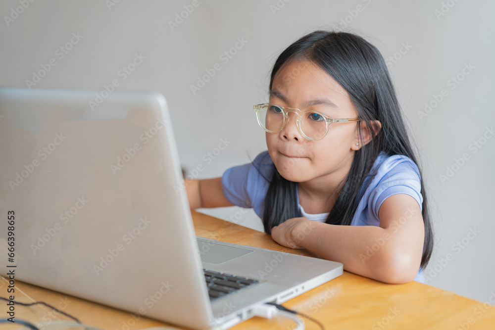 Portrait of little girl using laptop, student typing on keyboard looking at screen, watching webinar, online course, doing homework, playing games on the computer in the living room.