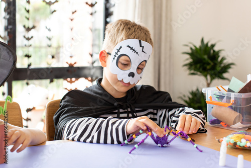 A cute boy in a carnival costume makes a funny spider with his own hands for Halloween.  photo