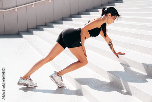 Fitness woman in sports clothing. Sexy young beautiful model athlete doing fitness workout. Female making exercises in the street at sunny day. Stretching out before training. at stairs
