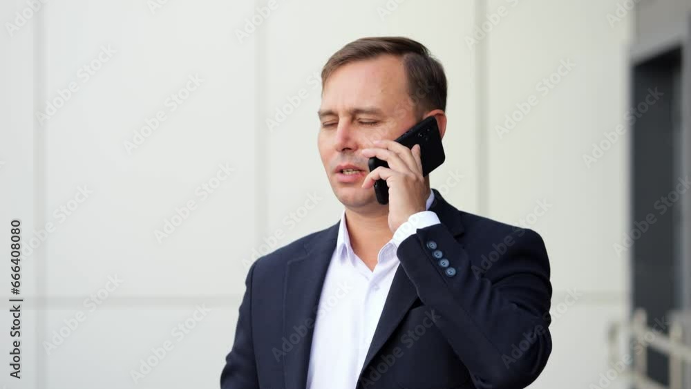 Confident adult businessman dressed in suit stands outdoors talking on phone. Concerned mature man in formal suit talks with interest on smartphone Confident adult businessman dressed in suit stands outdoors talking on phone. Concerned mature man in formal suit talks with interest on smartphone