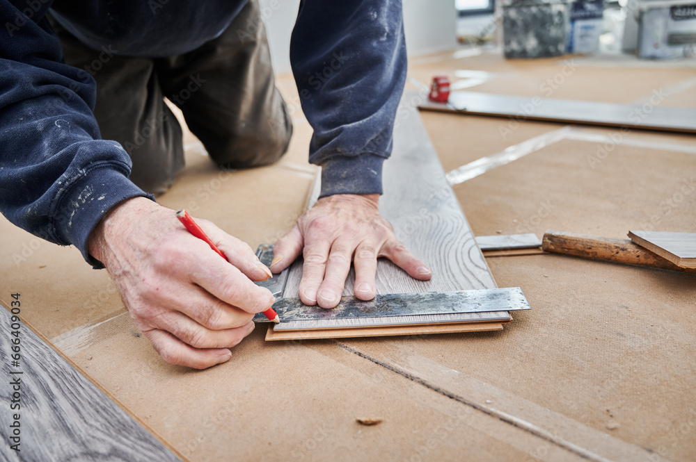 Close up of man hands using metal ruler and pencil while drawing line on laminate wooden board. Male construction worker measuring laminate panel for floor installation. Flooring renovation concept. Close up of man hands using metal ruler and pencil while drawing line on laminate wooden board. Male construction worker measuring laminate panel for floor installation. Flooring renovation concept.