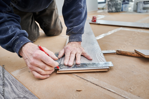 Close up of man hands using metal ruler and pencil while drawing line on laminate wooden board. Male construction worker measuring laminate panel for floor installation. Flooring renovation concept.