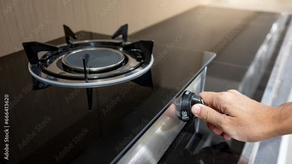 Male hand turning switch knob on modern gas stove in kitchen showroom. Cooking appliances in the domestic kitchen. Home improvement and House interior design concepts