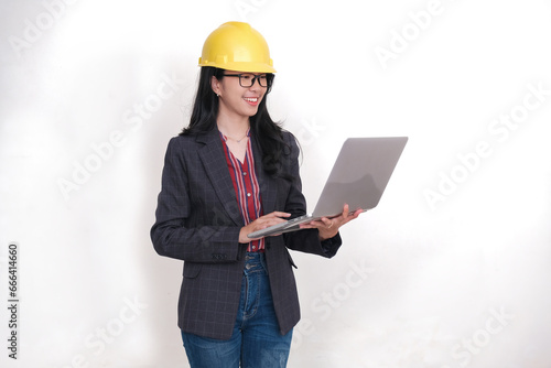 Female project engineer wearing yellow hard hat, standing and checking project data using computer in her hand photo
