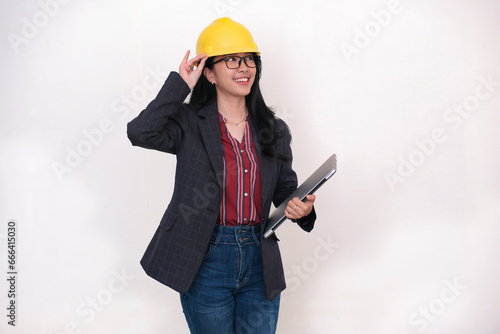 Female engineer fixing her yellow safety hard hat and holding a laptop in hand photo