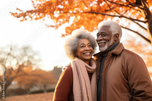 An elderly dark-skinned couple, a man and a woman, hugging in an autumn park. They look at each other with a loving gaze. Seniors dating. Relationships in old age. Love and romance.