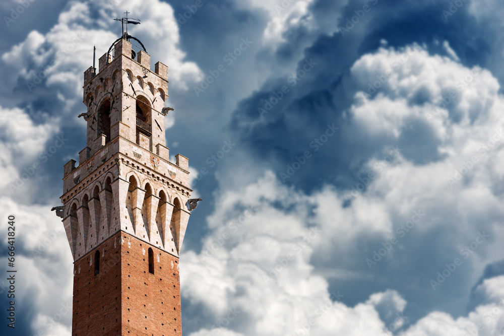 Close-up of Torre del Mangia (Tower of Mangia) in Piazza del Campo in Siena downtown, Tuscany, Italy, Europe. Against a sky with beautiful cumulus clouds.