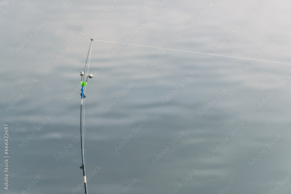 Part of a fishing rod with a stretched fishing line against the background of water. Background for the theme of recreation on fishing.