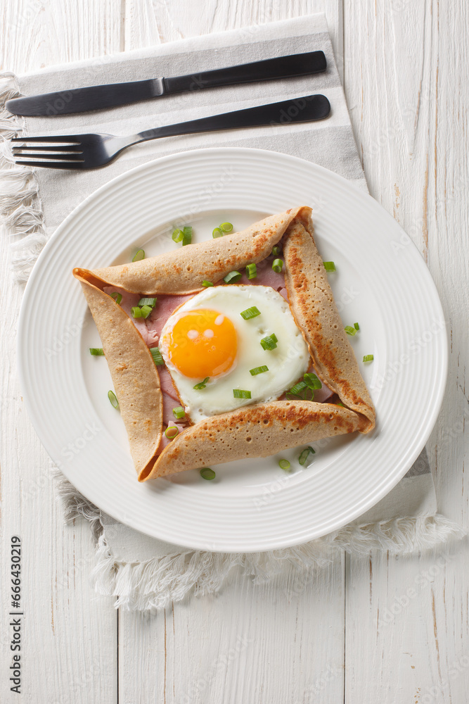 Homemade buckwheat crepe galette with egg, ham and green onion closeup on the plate on the table. Vertical top view from above Homemade buckwheat crepe galette with egg, ham and green onion closeup on the plate on the table. Vertical top view from above