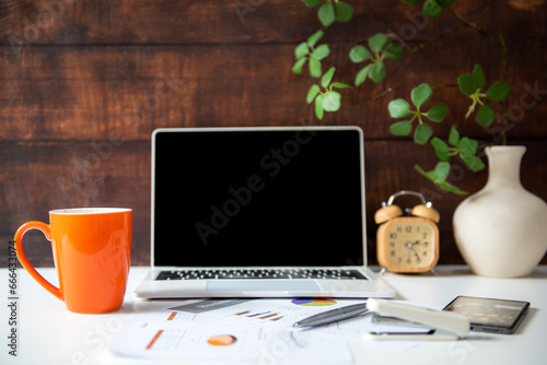 Business workplace with laptop and graphs finance diagrams and orange cup coffee drink. Old wood background. Business Object Concept