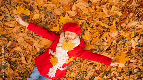 An overhead view of a caucasian girl in a red coat and beret lies on yellow foliage. Walk in the park in autumn. 
