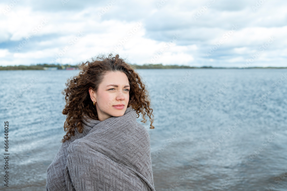 Contemplative woman with curly hair wrapped in shawl at water Contemplative woman with curly hair wrapped in shawl at water