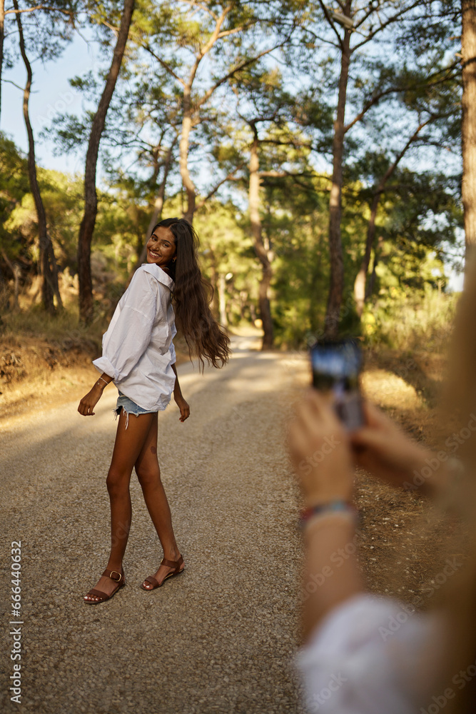 Woman photographing teenage daughter standing on road in forest Woman photographing teenage daughter standing on road in forest