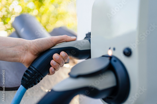 Hand of woman holding electric plug at charging station photo