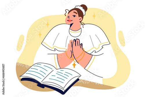 Woman nun stands near open bible and holds chain with christian cross in hands making prayer gesture