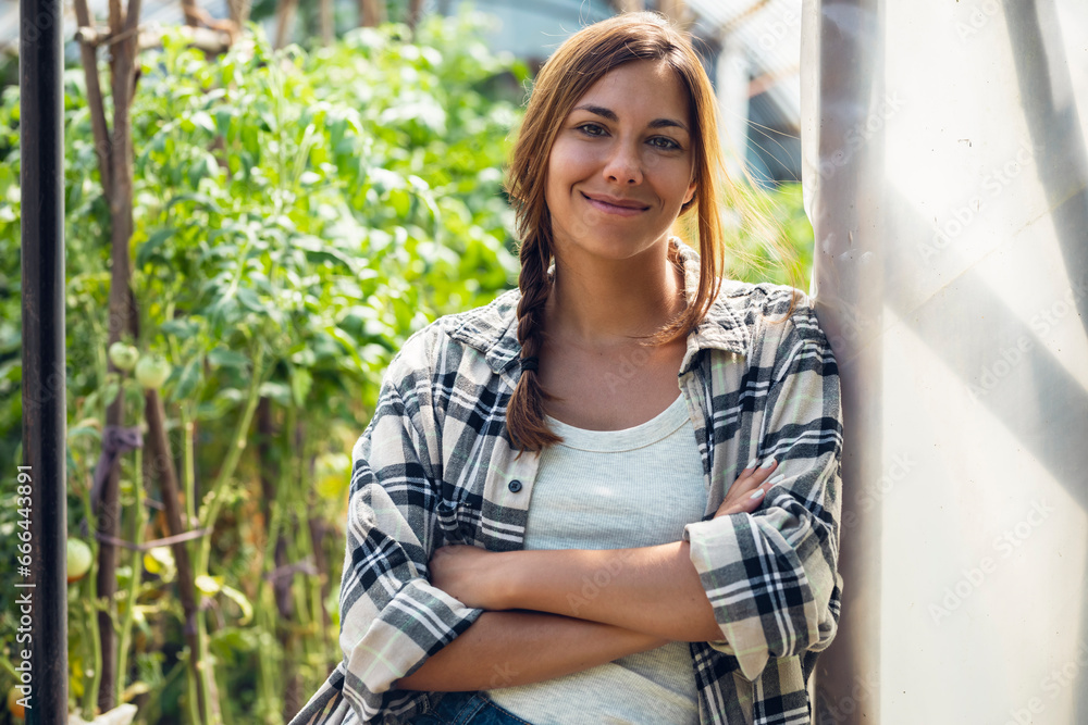 Smiling young farmer with arms crossed standing at greenhouse doorway Smiling young farmer with arms crossed standing at greenhouse doorway