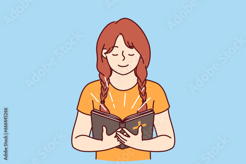 Little girl with bible in hands studies prayers and gospel before going to christian church. Happy child believer in catholic religion holds bible illuminating face and smiles feeling support of lord