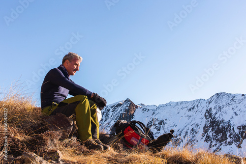 Contemplative man sitting with backpack on mountain in winter photo