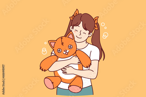Little girl holds plush cat and smiles and rejoices at presence of favorite toy. Positive child with toy given by mom or dad enjoys hugging kitten for concept of happy childhood for daughter