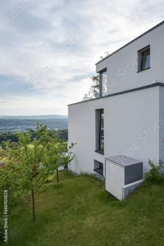 external unit of an air source heat pump in front of a modern low energy house surrounded by nature photo