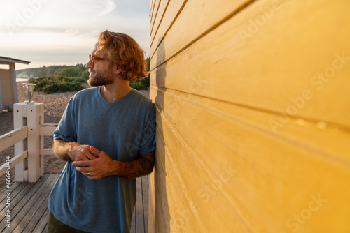 Young man with blond hair leaning on beach hut